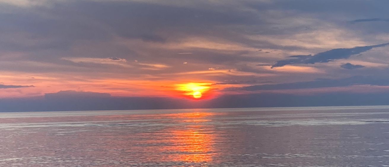 Ein Sonnenuntergang über dem Meer, mit warmen orangefarbenen und rosa Farbtönen, die den Himmel erhellen und sich auf der Wasseroberfläche spiegeln.