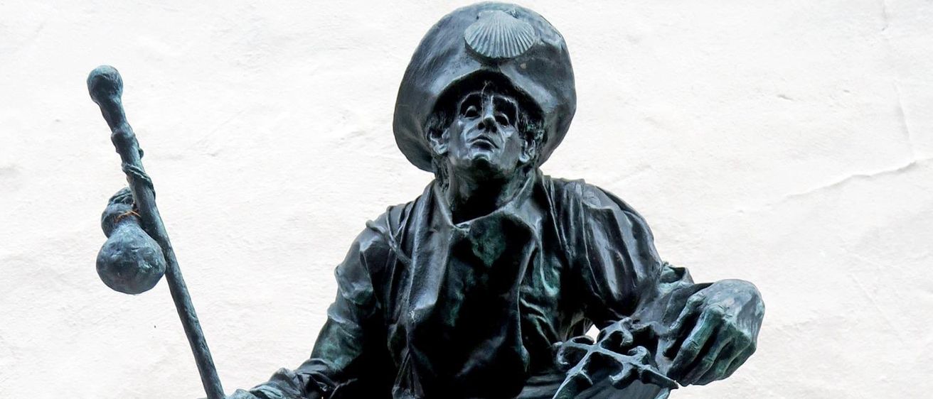 Bronzestatue einer sitzenden Figur, die einen Schild und einen Stab hält, auf einem Steinsockel, mit dem Namen 'Im Aufbruch' eingraviert.