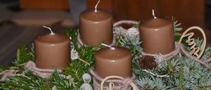 Ein Kranz mit vier braunen Kerzen und Tannennadeln, verziert mit zwei Holzschildern, die 'Fried' und 'Liebe' sagen. Er steht auf einem Holztisch.