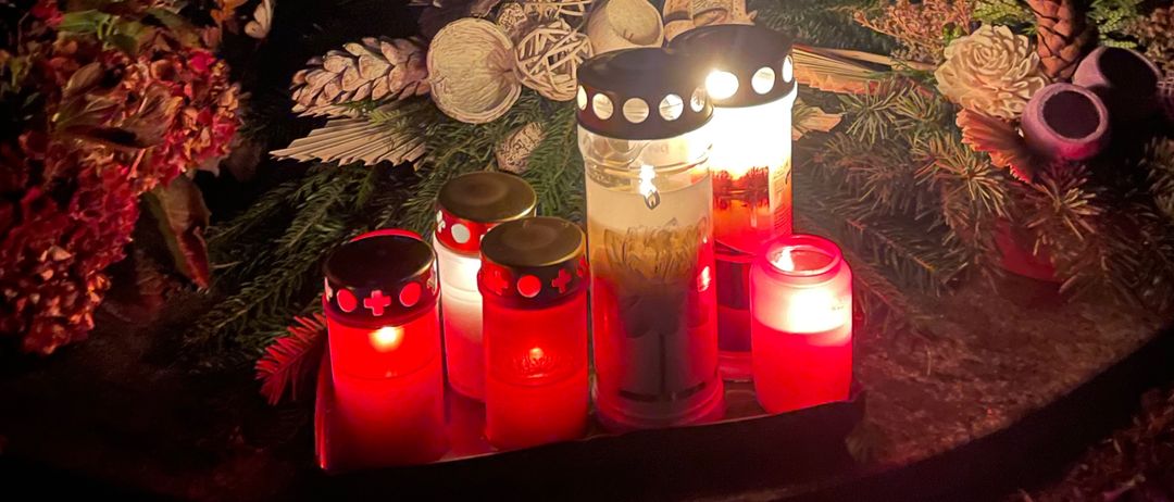 Ein Gedenkort mit brennenden Kerzen und Blumen. Die Inschrift an der Wand lautet 'St. Monika'.