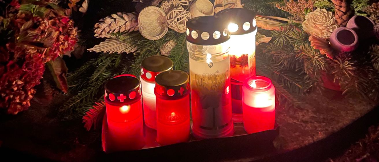 Ein Gedenkort mit brennenden Kerzen und Blumen. Die Inschrift an der Wand lautet 'St. Monika'.