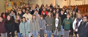 Eine Gruppe von Schülern und Lehrern steht in einer Kirche und lächelt für ein Foto. Der Altar ist im Hintergrund mit Kerzen.