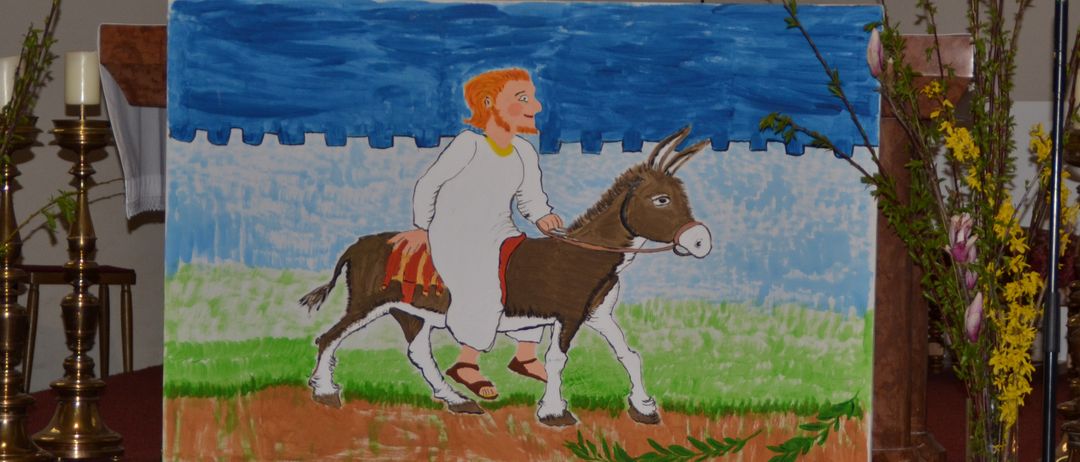 Ein Bild eines Mannes, der auf einem Esel reitet, ausgestellt auf einer Bühne mit Mikrofon und Blumen.