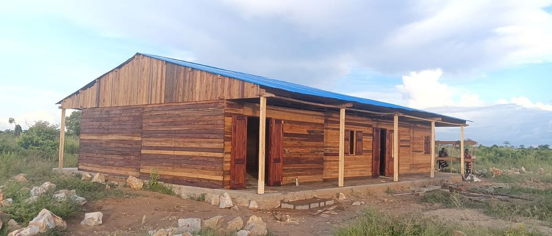 Ein Holzgebäude mit einem blauen Dach und Holztüren, umgeben von Steinen und Gras.