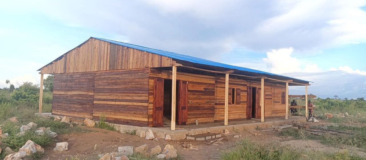 Ein Holzgebäude mit einem blauen Dach und Holztüren, umgeben von Steinen und Gras.