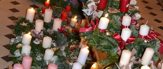 Ein Gang, geschmückt mit mehreren Kränzen und Kerzen, jeder Kranz besteht aus grünen Blättern, roten Bändern und einer Mischung aus weißen und roten Kerzen. Der Boden hat ein schwarz-weißes Schachbrettmuster.