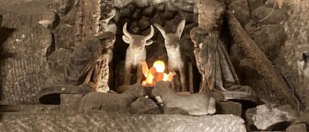 Eine steinerne Krippe mit Krippe, Stern und Figuren von Jesus, Maria, Josef und Tieren, in einer höhlenartigen Umgebung.