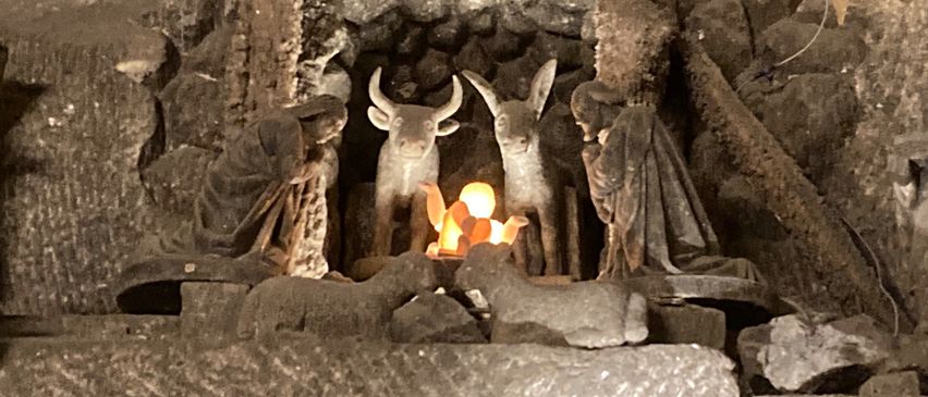 Eine steinerne Krippe mit Krippe, Stern und Figuren von Jesus, Maria, Josef und Tieren, in einer höhlenartigen Umgebung.