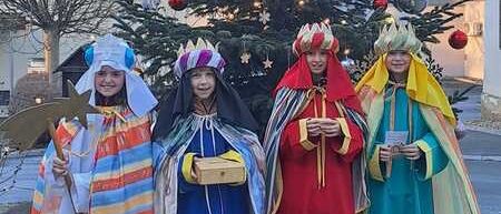 Vier Menschen in traditionellen Kostümen stehen vor einem geschmückten Weihnachtsbaum und lächeln in die Kamera.