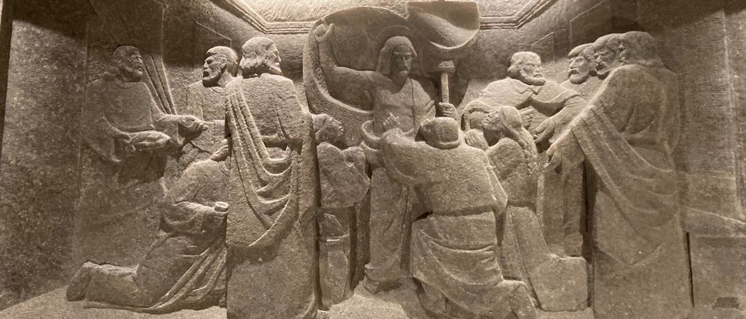 Eine Steinschnitzerei, die eine Szene mit mehreren Personen darstellt, möglicherweise ein religiöses oder historisches Ereignis, in einer antiken Umgebung mit kunstvollen Verzierungen darüber.