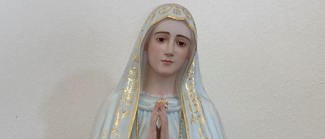 Eine Statue einer Frau mit einem weißen und goldenen Gewand und Schleier, die mit einem Rosenkranz in den Händen betet.