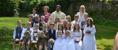 Eine Gruppe von Kindern und Erwachsenen posiert für ein Foto in einem Garten mit Brot in den Händen. Ein Priester steht unter ihnen.