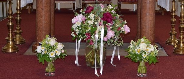 Ein Altar mit weißen Kerzen, einem Blumenzentrum und einem Gemälde darüber in einer Kirche.
