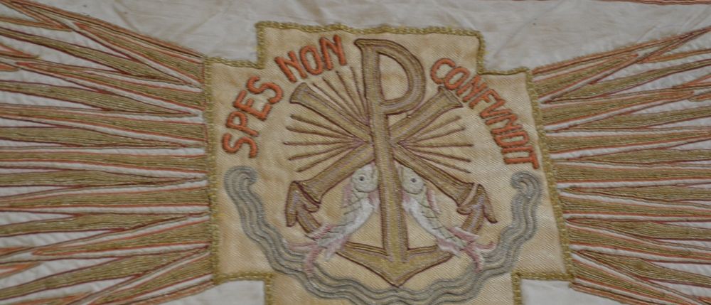 Gestickte Banner mit einem Anker, Fischen und Lichtstrahlen. Lateinische Worte 'SPES NON CONFUNDIT' sind in der Mitte gestickt.