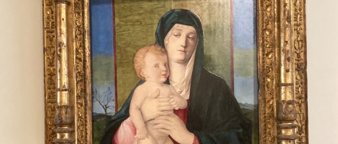 Ein gerahmtes Gemälde zeigt eine gelassene Jungfrau Maria, die ein junges Jesuskind in traditioneller mittelalterlicher Kleidung hält. Der Hintergrund zeigt eine Landschaft mit Bäumen.