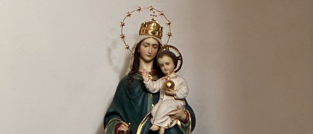 Eine Statue der Jungfrau Maria, die das Jesuskind hält, geschmückt mit einer Krone und auf einem Halbmond stehend.