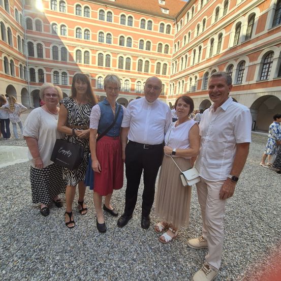 Eine Gruppe von sechs Personen, drei Männer und drei Frauen, steht vor einem historischen Gebäude und lächelt für ein Foto.