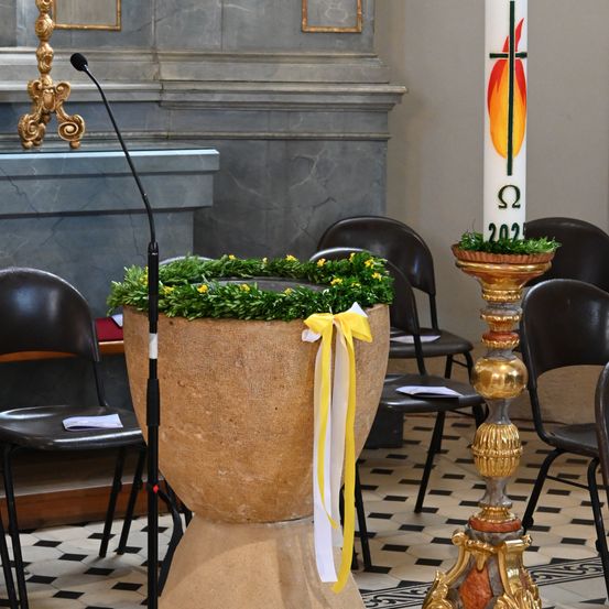 Ein Altar in einer Kirche mit einem dekorierten Taufbecken und einem Mikrofon, dahinter steht eine Kerze.