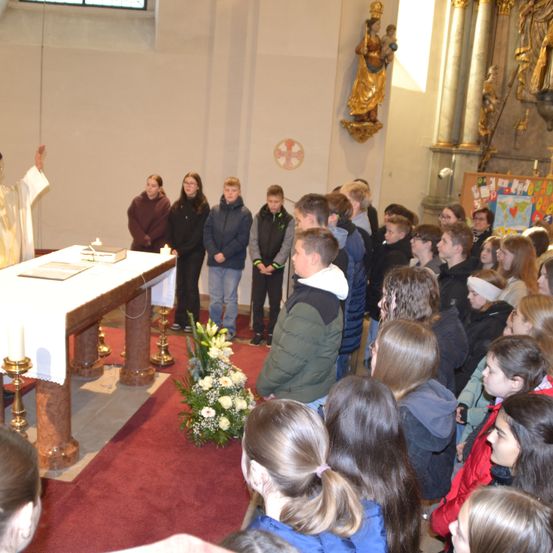 Ein Priester leitet eine Zeremonie in einer Kirche, während eine Gruppe von Menschen zuschaut, Blumen und Kerzen auf dem Altar.