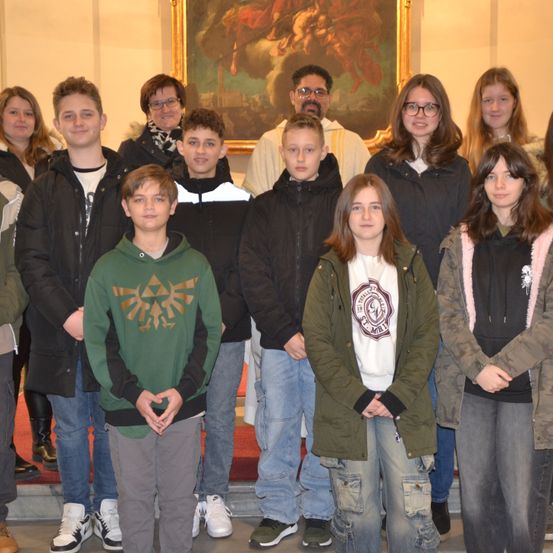 Eine Gruppe junger Menschen und Erwachsene posiert für ein Foto vor einem großen Gemälde an der Wand.