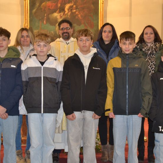 Eine Gruppe junger Jungen und Frauen steht vor einem Priester und einem Gemälde.