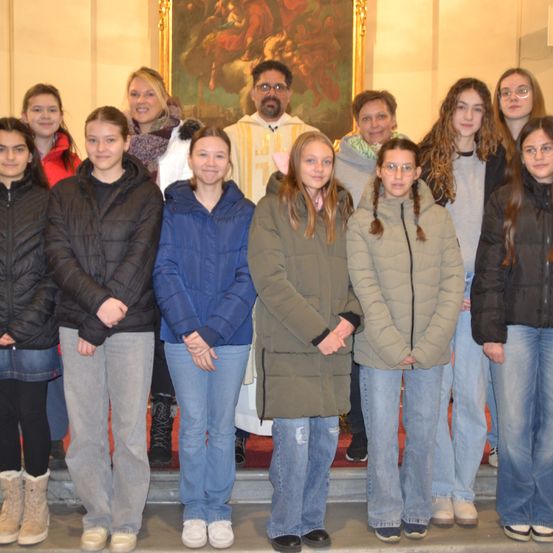 Eine Gruppe von Schülern und ein Priester posiert für ein Foto in einer Kirche mit einem Gemälde im Hintergrund.