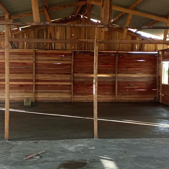 Ein leerer Raum mit Holzwänden und -balken, einem Betonboden und einem kleinen Fenster, das Sonnenlicht hereinlässt.