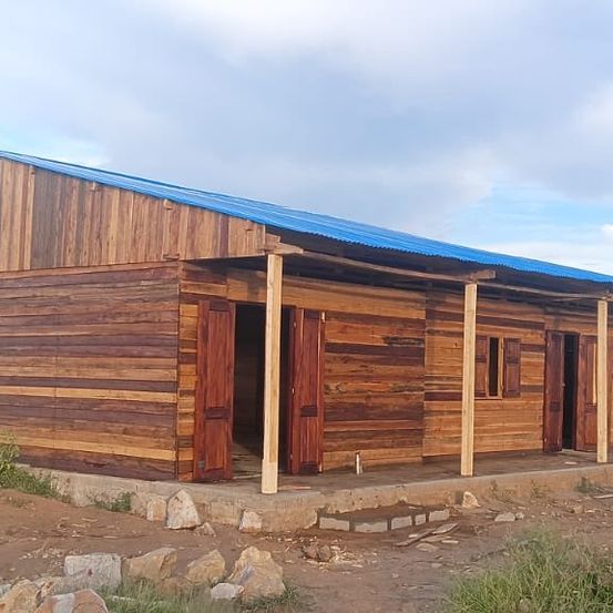 Ein Holzhaus mit blauem Dach, gelegen in einem ländlichen Gebiet mit einem unfertigen Betonvorplatz und einigen Steinen darum herum.