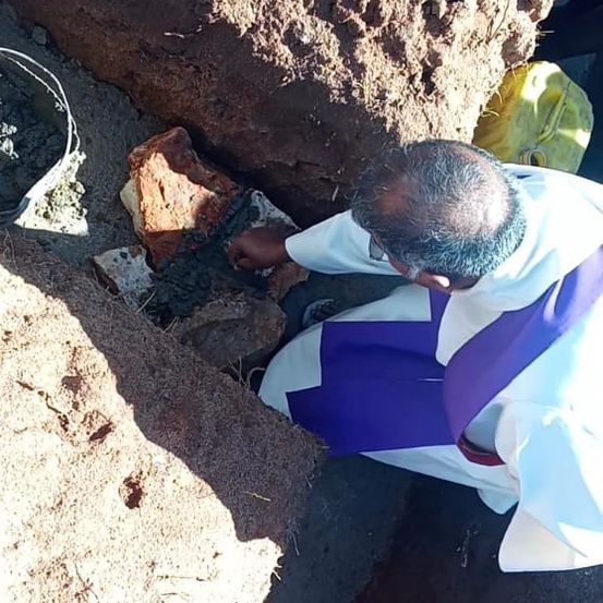 Ein Priester kniet und hält einen Stein in der Hand, möglicherweise für ein religiöses Ritual.