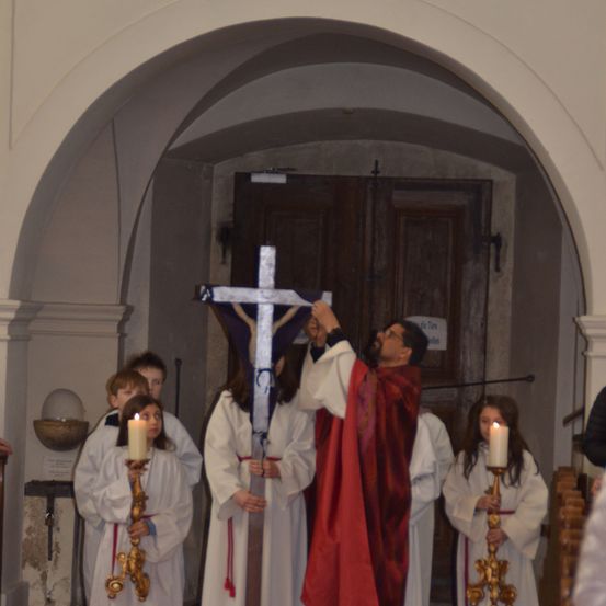 Eine religiöse Zeremonie in einer Kirche mit mehreren Personen, die Kerzen und ein Kreuz halten.
