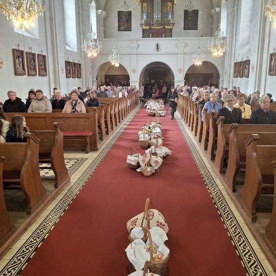 Eine Kirche mit vielen Menschen auf Bänken, Körben auf einem roten Teppich, Kronleuchtern und Gemälden.