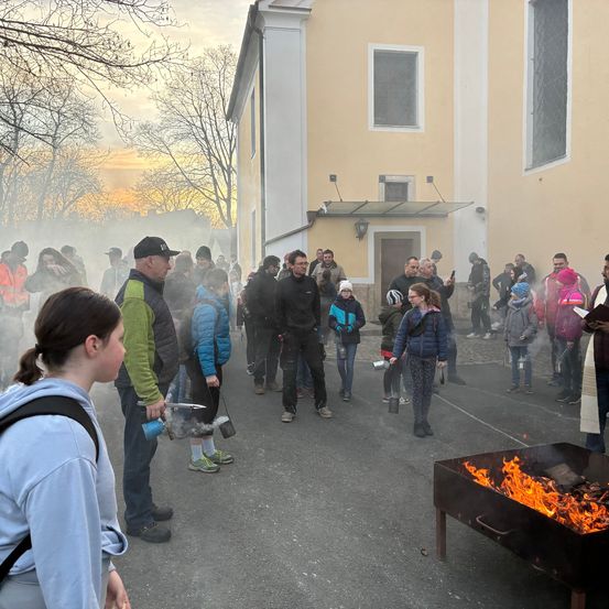 Eine Menschenmenge in Winterkleidung versammelt sich um ein brennendes Feuer, wahrscheinlich zur Wärme, vor einem Gebäude.