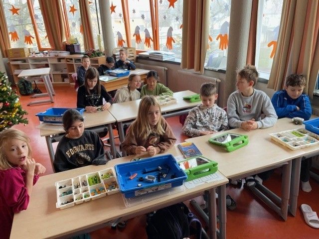 Schüler arbeiten in einem Klassenzimmer mit Weihnachtsdekoration und sternenförmigen Fenstern an einem Projekt an ihren Schreibtischen.