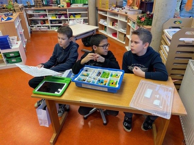 Drei Jungen sitzen an einem Tisch in einem Klassenzimmer und beschäftigen sich mit einem Lego-Set.