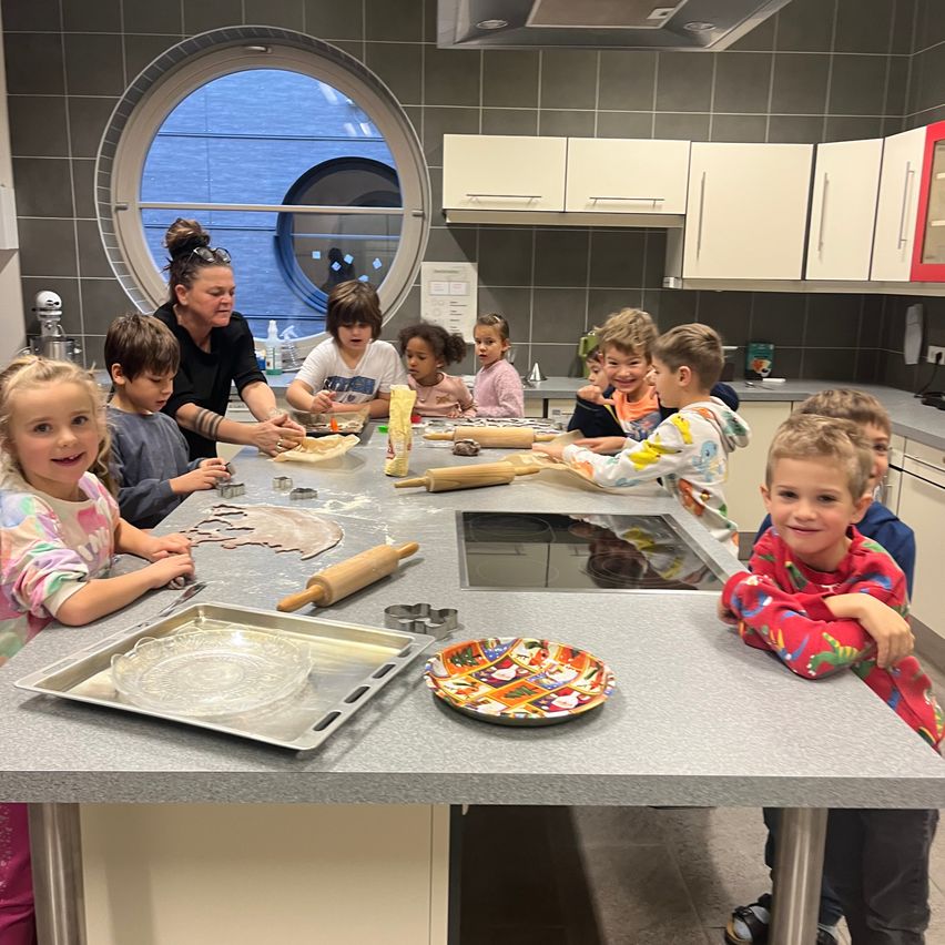 Kinder und eine Frau sind in einer Küche und bereiten Teig auf einem Arbeitstisch mit verschiedenen Utensilien und Dekorationen zu.