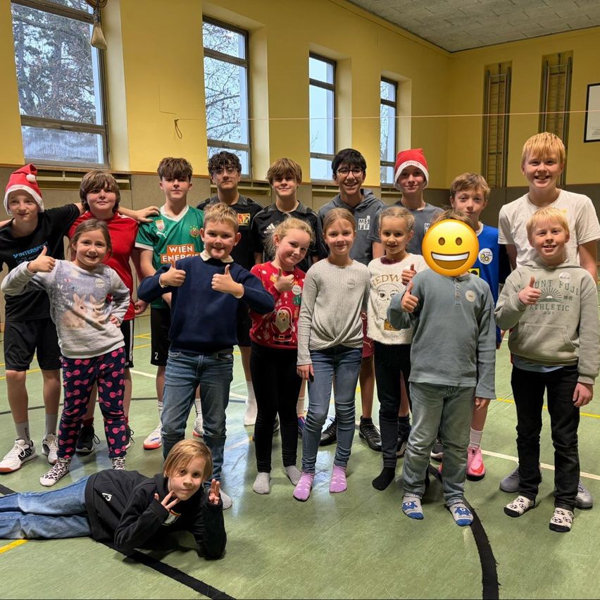 Eine Gruppe von Kindern und Jugendlichen posiert für ein Foto in einer Turnhalle. Sie lächeln und zeigen Daumen hoch. Der Boden hat gelbe Markierungen.