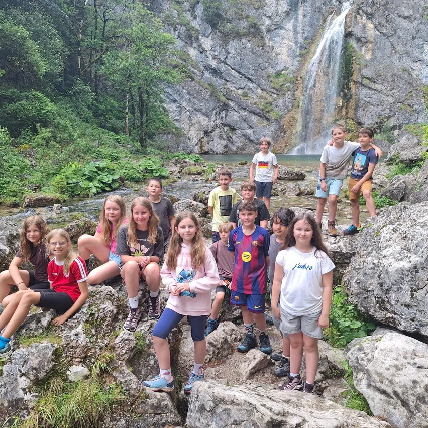 Eine Gruppe von Kindern und Jugendlichen posiert für ein Foto auf Felsen in der Nähe eines Wasserfalls.