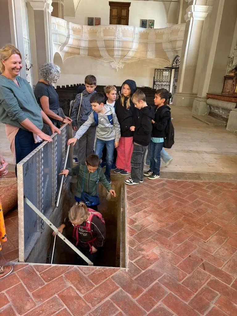 Eine Gruppe von Kindern und Erwachsenen versammelt sich um ein Loch im Boden einer Kirche.