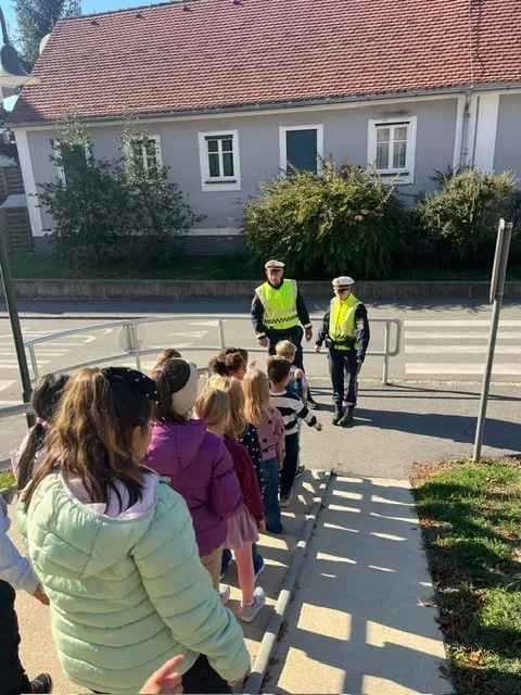 Zwei Verkehrspolizisten helfen einer Gruppe von Kindern beim Überqueren der Straße vor einem Haus.