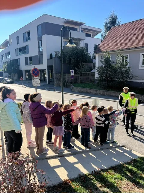 Eine Gruppe von Kindern steht auf dem Bürgersteig, vor ihnen stehen zwei Polizeibeamte in Warnwesten.