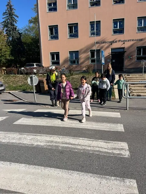 Eine Gruppe von Kindern, begleitet von einem Verkehrspolizisten, überquert die Straße an einem Zebrastreifen.