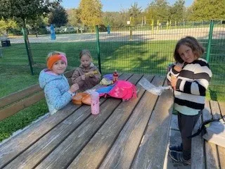 Drei junge Mädchen sitzen an einem Picknicktisch im Park. Sie essen und trinken aus ihren Lunchboxen.