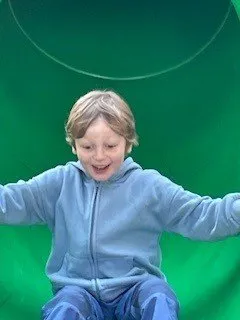 Ein junger Junge rutscht einen grünen Rutschen hinunter, seine Arme ausgestreckt und ein fröhliches Gesichtsausdruck.