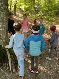 Eine Gruppe von Kindern erkundet einen Waldpfad. Sie stehen um einen Baum herum und scheinen in ein Gespräch vertieft zu sein.