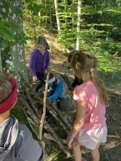 Eine Gruppe von Kindern spielt im Wald. Sie bauen eine Unterkunft aus Stöcken und Ästen.