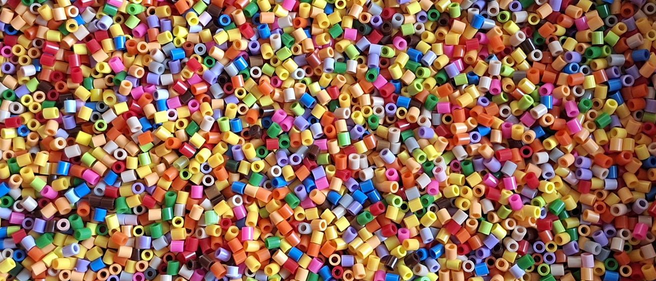 Ein Nahaufnahme einer bunten Anordnung von zylindrischen Perlen, jede mit einem Loch in der Mitte, verstreut in verschiedenen Größen und Farben.