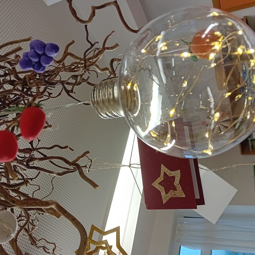 A large transparent light bulb hangs from the ceiling, decorated with small lights and ornaments. Below it, there is a star-shaped decoration on a red background.