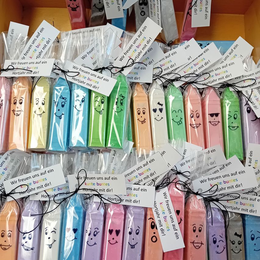 A collection of colorful chalk sticks with cheerful faces, each wrapped in plastic and labeled with a birthday message. The colors range from pink to blue, and they are neatly arranged in a row.