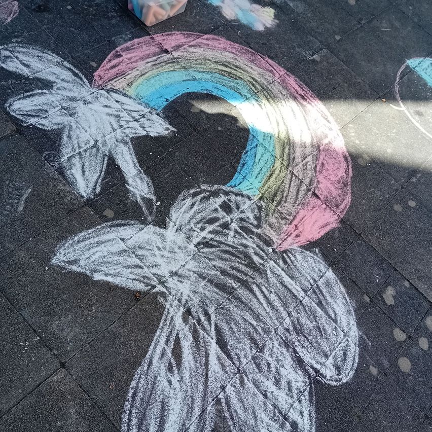 A chalk drawing of a butterfly with wings spread out on a sidewalk, next to a rainbow.
