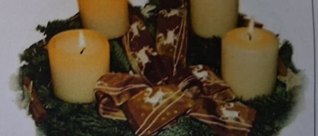 Vier Kerzen sind in einem Kreis angeordnet, möglicherweise für einen Adventskranz, geschmückt mit grünen Blättern und einem braunen Band mit weißen Designs.